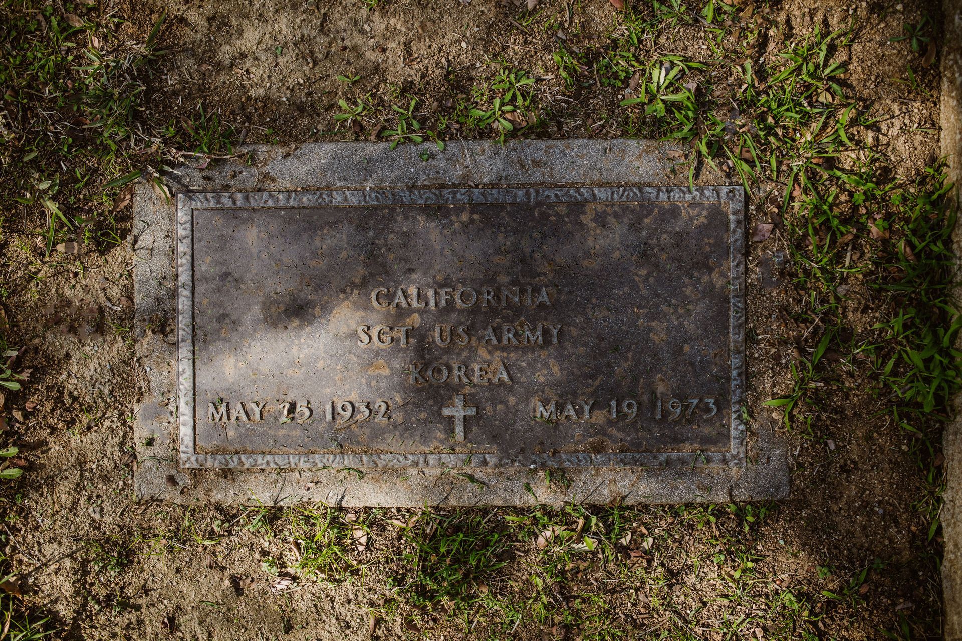 Weathered gravestone in grass, with engraved cross and faded inscriptions.