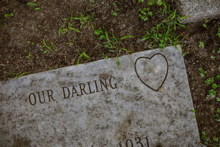 Gravestone engraved “OUR DARLING” with a heart, set among grass and dirt.
