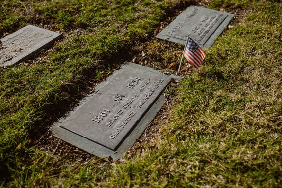 Gravestones in a grassy cemetery, one marked with a small American flag.