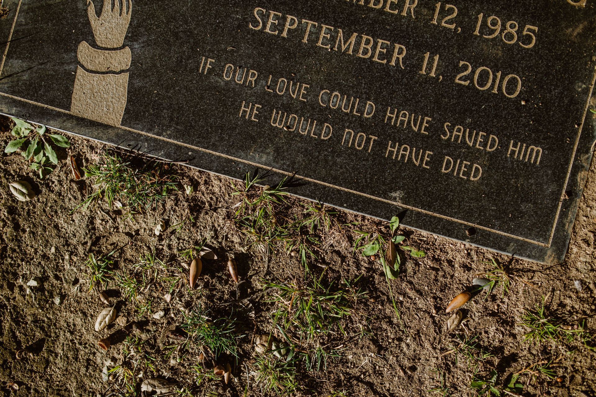Close-up of a tilted grave marker engraved with a hand and the words “If God loves…”