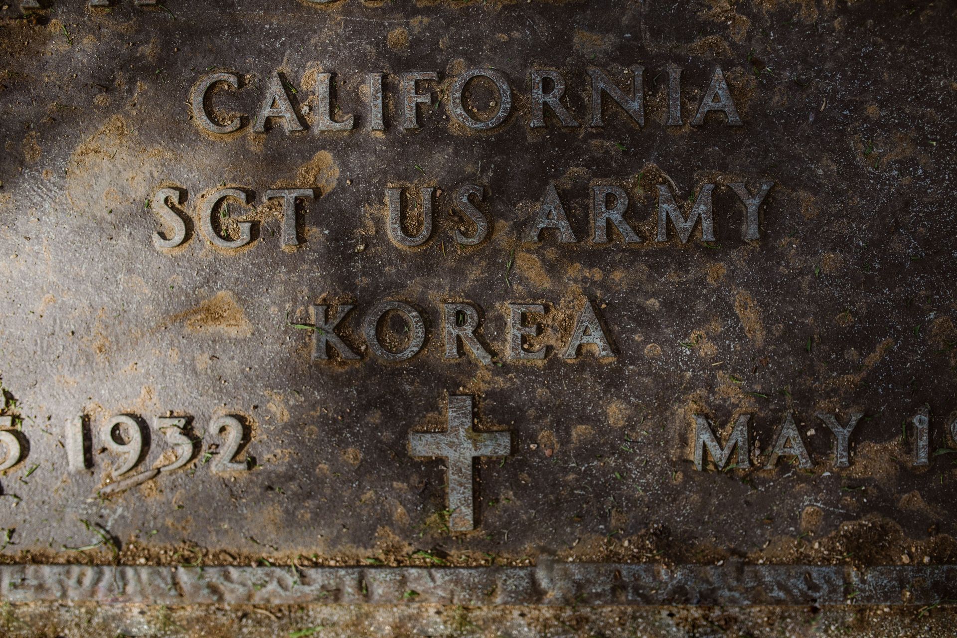 Weathered stone grave marker reading “California,” “Sgt. US Army,” and “Korea,” with a cross and date fragments.