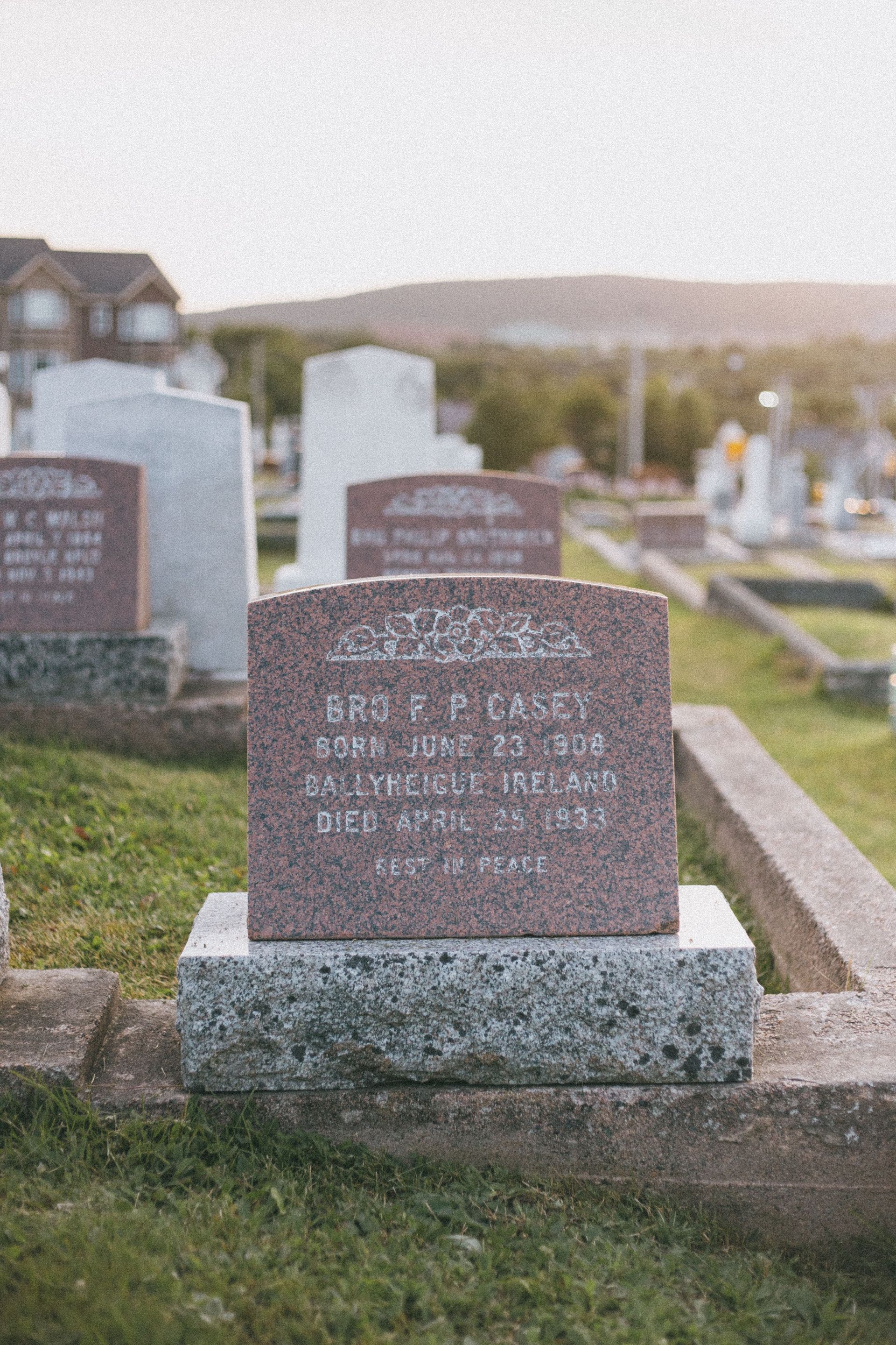 Gravestone in a cemetery with a house in the background and hills beyond
