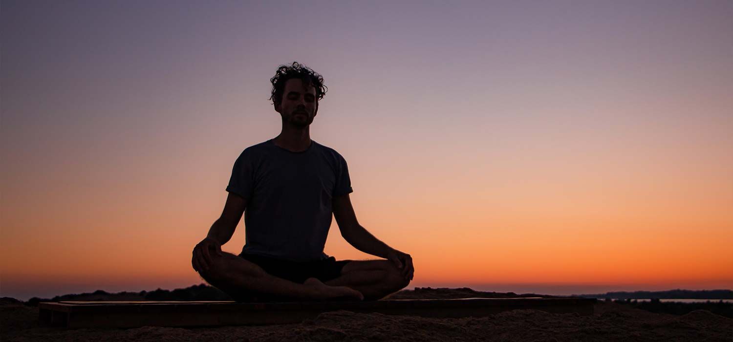 Man meditating at sunset on Issos Beach during a yoga retreat in Corfu