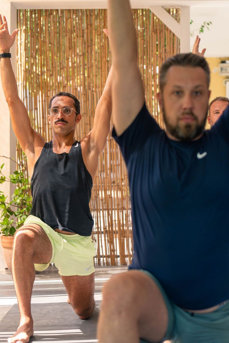 Yoga teacher guiding a student through a low lunge pose at the Corfu retreat