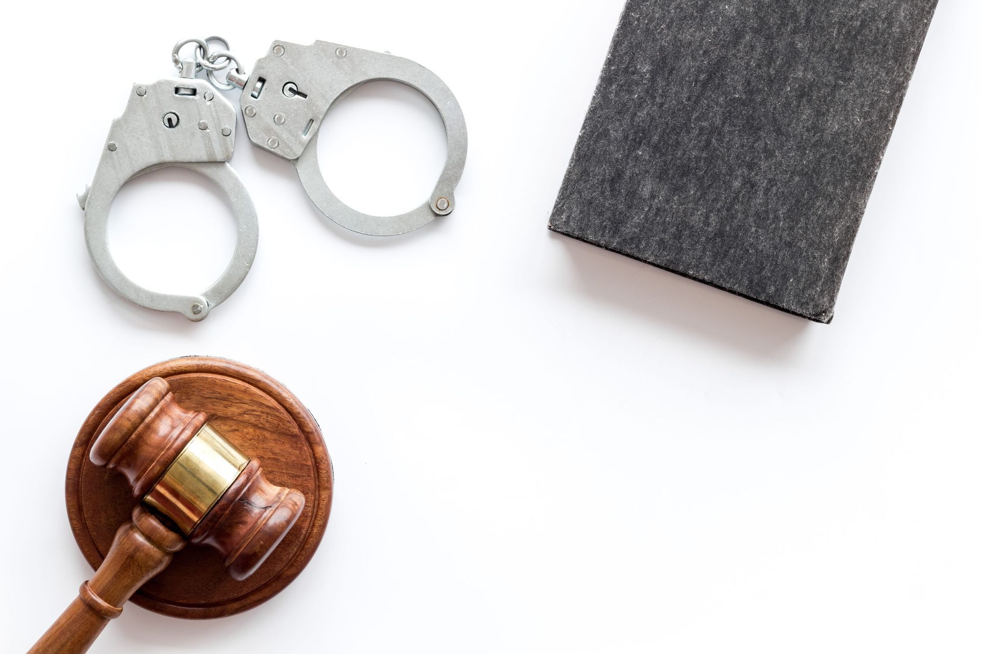Handcuffs, a judge’s gavel, and a black notebook on a white background