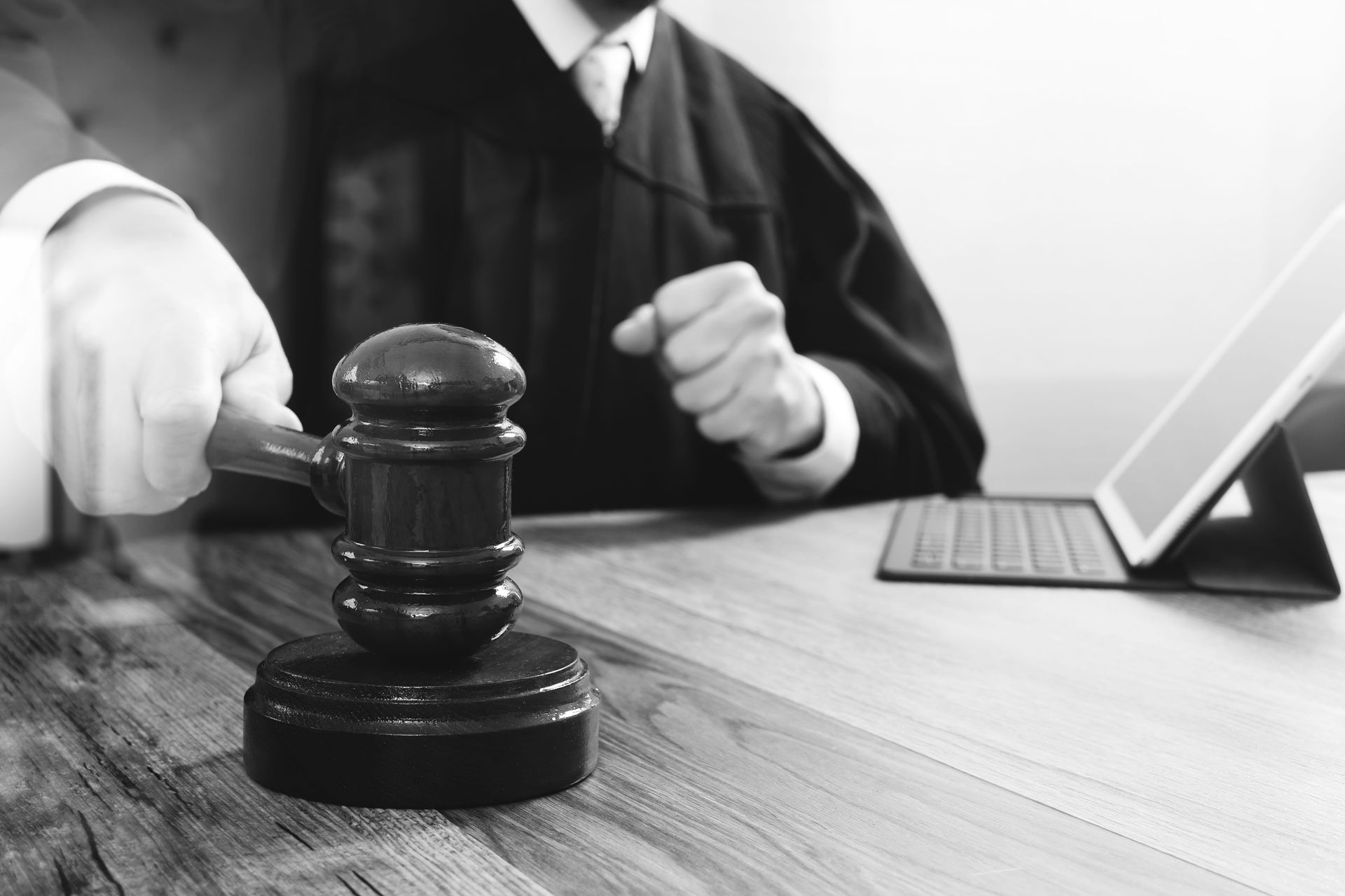 Judge’s gavel on a desk beside a laptop, with a person gesturing in the background.