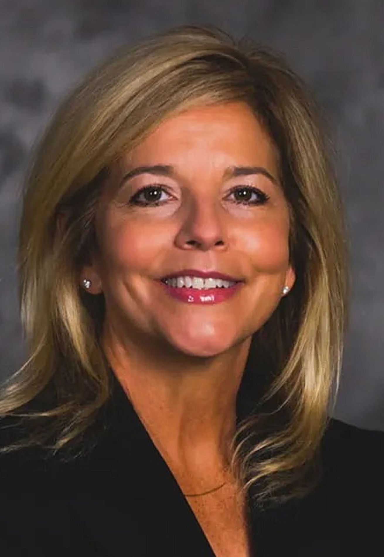 Smiling woman with blonde hair in a black blazer against a dark gray background