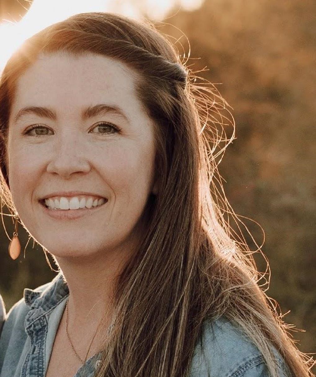 Smiling woman outdoors in warm sunlight, wearing a denim shirt.