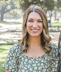 Smiling woman in a green floral dress standing outdoors with trees in the background