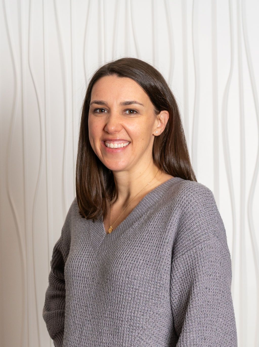 Smiling woman in a gray sweater standing before a white curtain backdrop