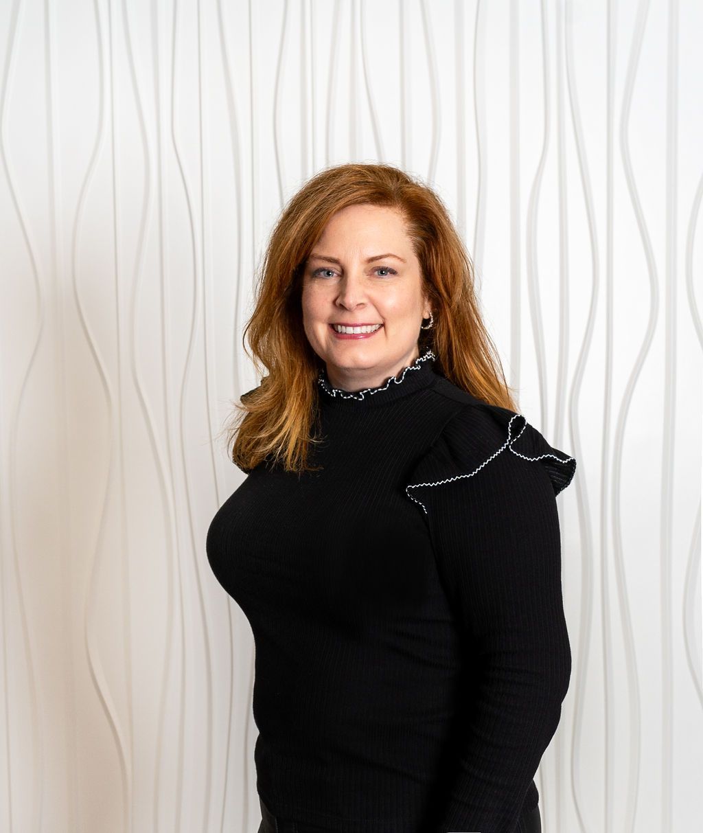 Smiling woman in a black top standing against a white wavy wall backdrop