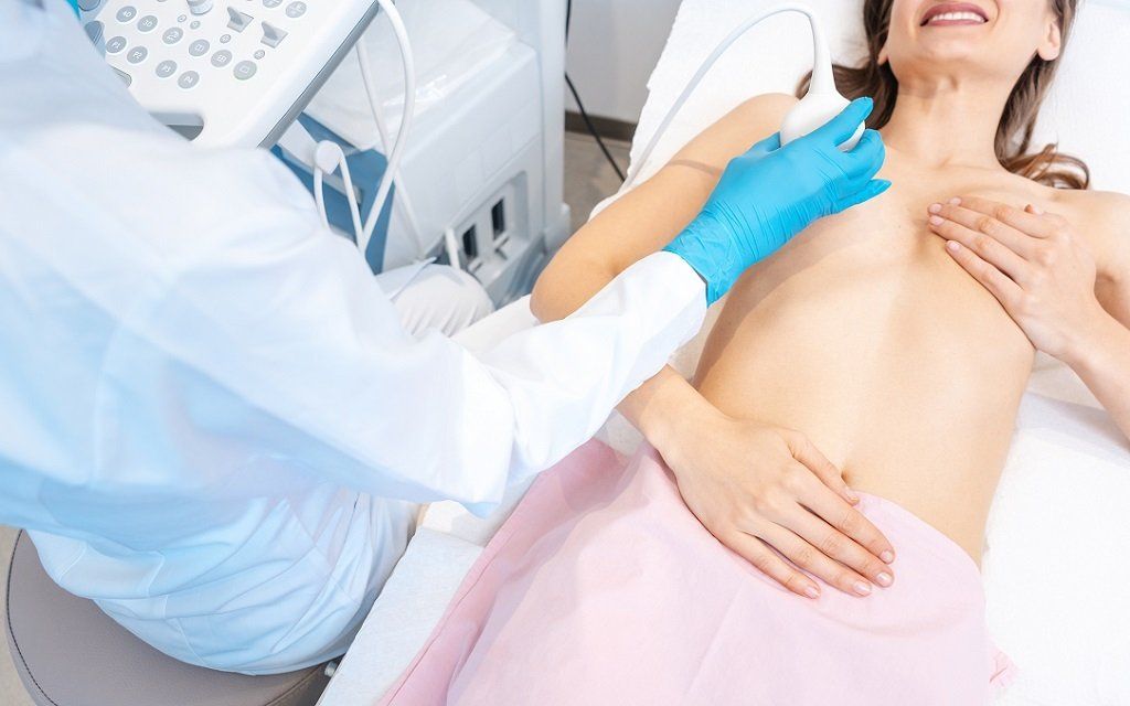 Medical exam of a patient on a bed while a clinician uses a handheld ultrasound probe on the chest