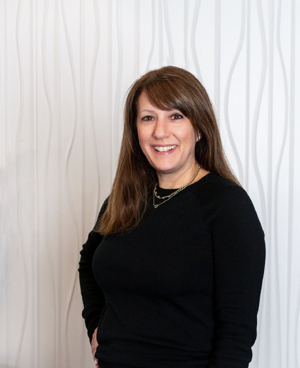 Smiling woman in a black top standing against a white textured wall