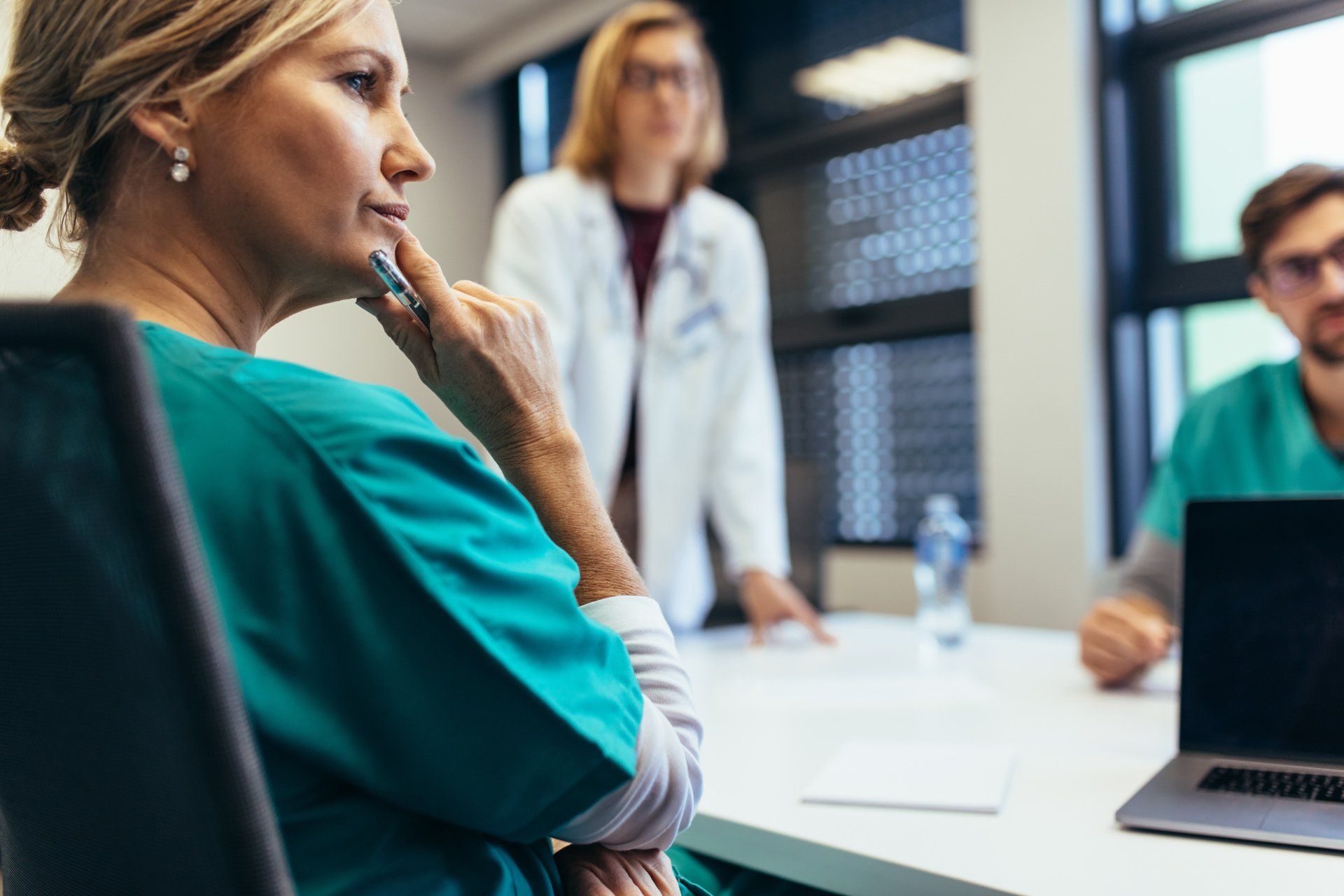 People in scrubs and lab coats in a meeting room, discussing over a laptop