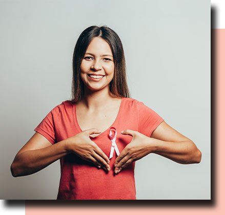 Woman in a coral shirt holding a pink breast cancer awareness ribbon in a heart shape
