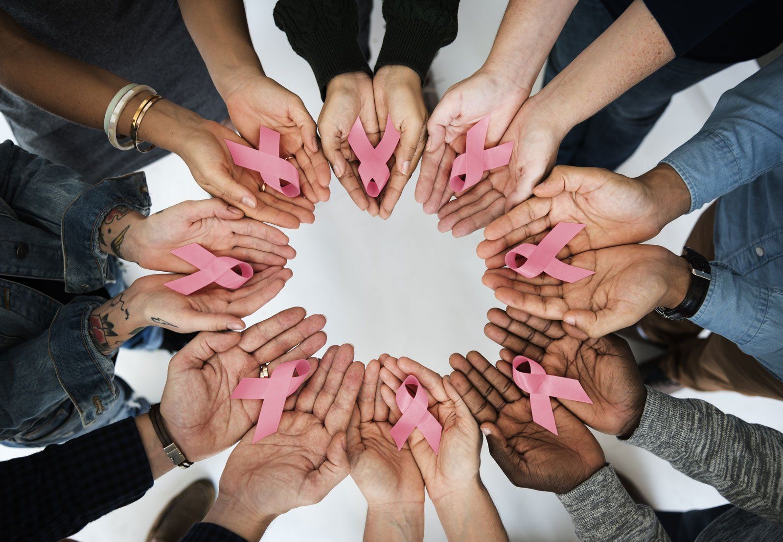 Hands holding pink ribbons in a circle on a white background, symbolizing breast cancer awareness