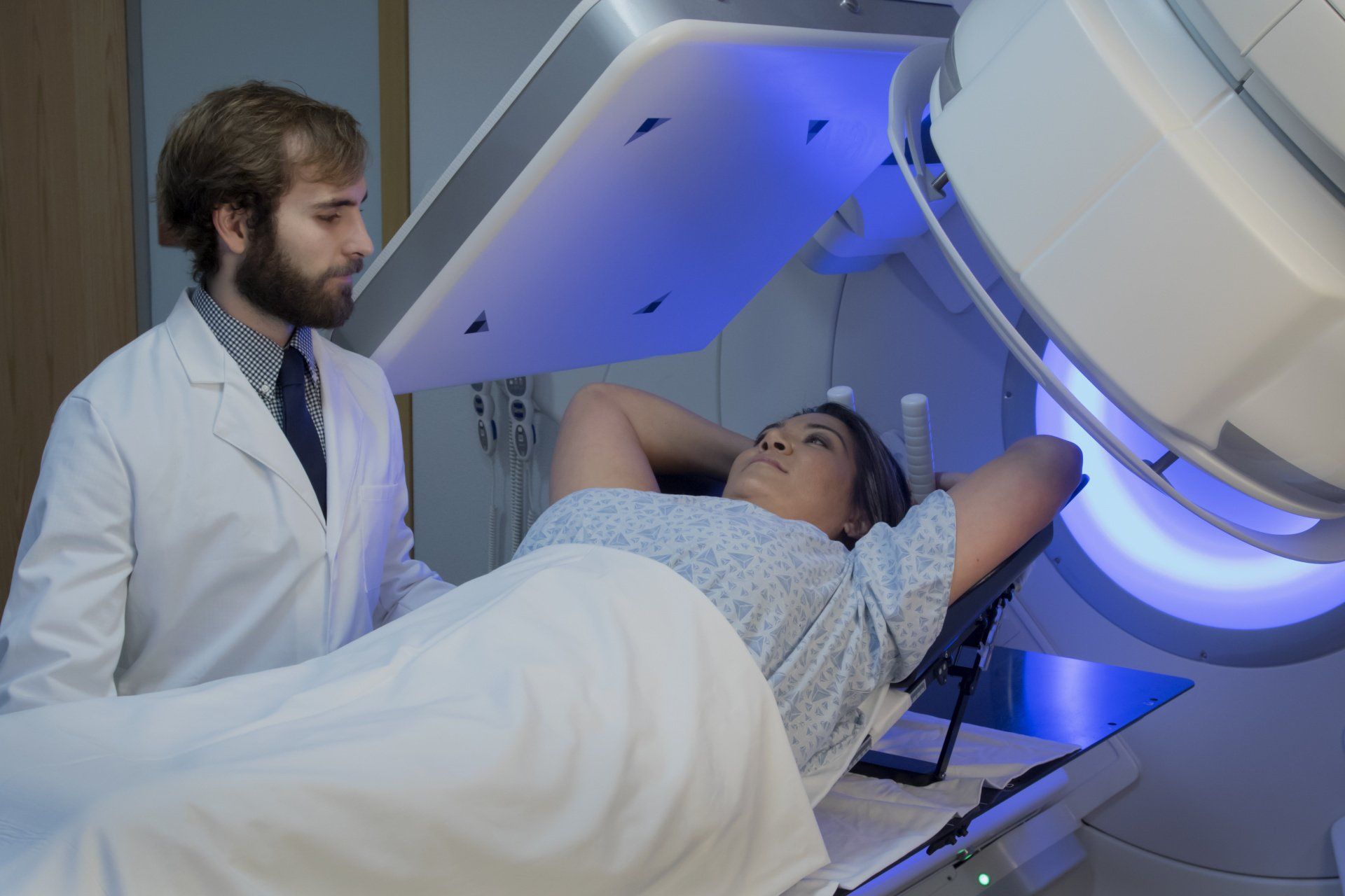 Patient lying in a blue-lit medical scanner as a doctor stands nearby