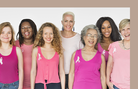 Group of people wearing pink shirts and ribbons, standing together and smiling against a neutral background