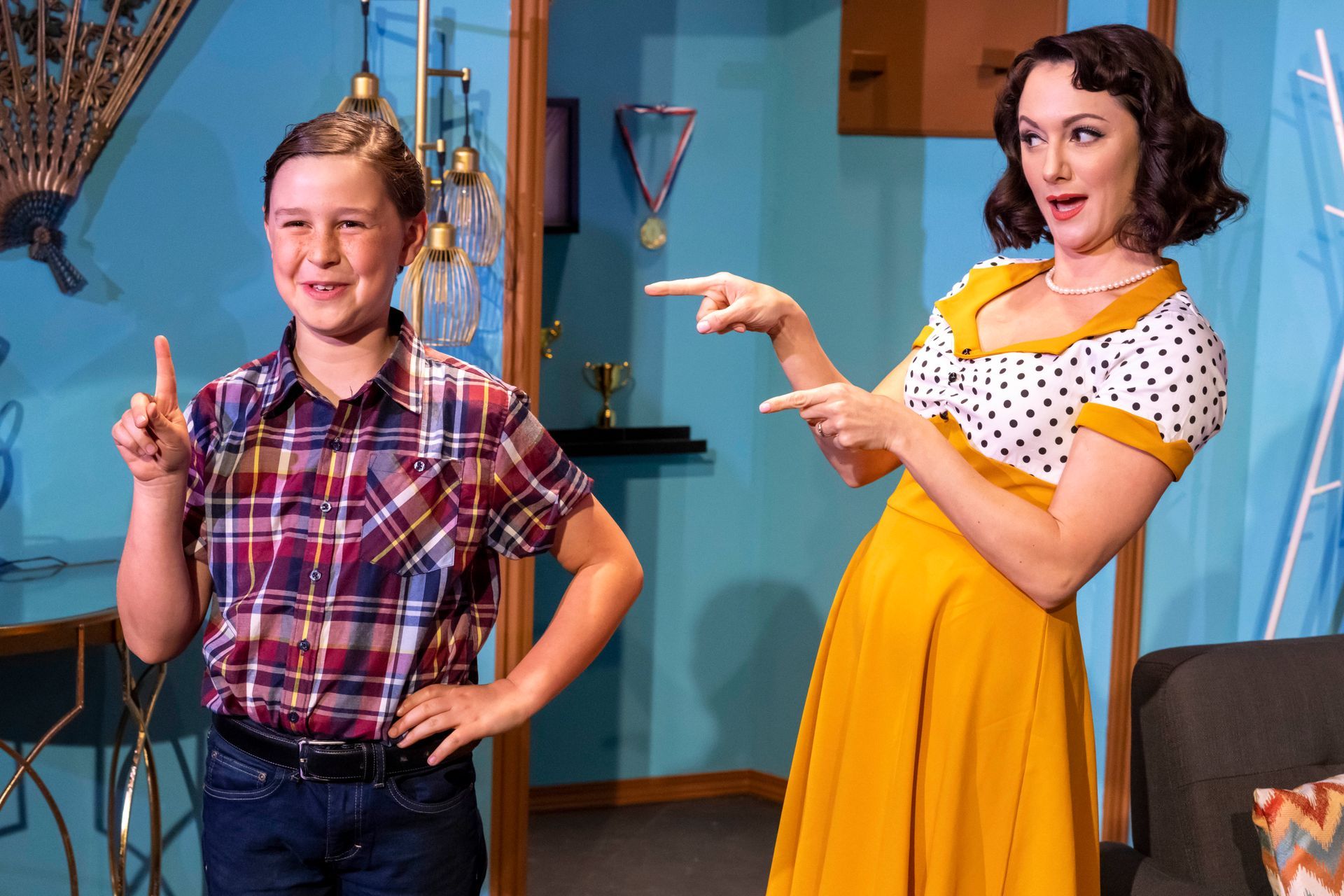 A woman in a yellow dress is pointing at a boy in a plaid shirt.