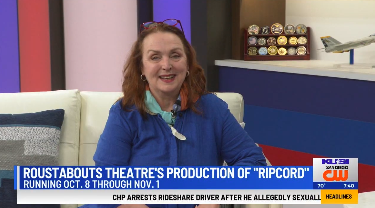 Woman speaking on a TV news set with a blue couch and on-screen headline about a theater production.