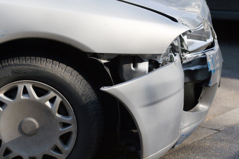 A Silver Car With a Damaged Bumper is Parked on the Side of the Road — Dynamic Dentz Smash Repair in North Nowra, NSW