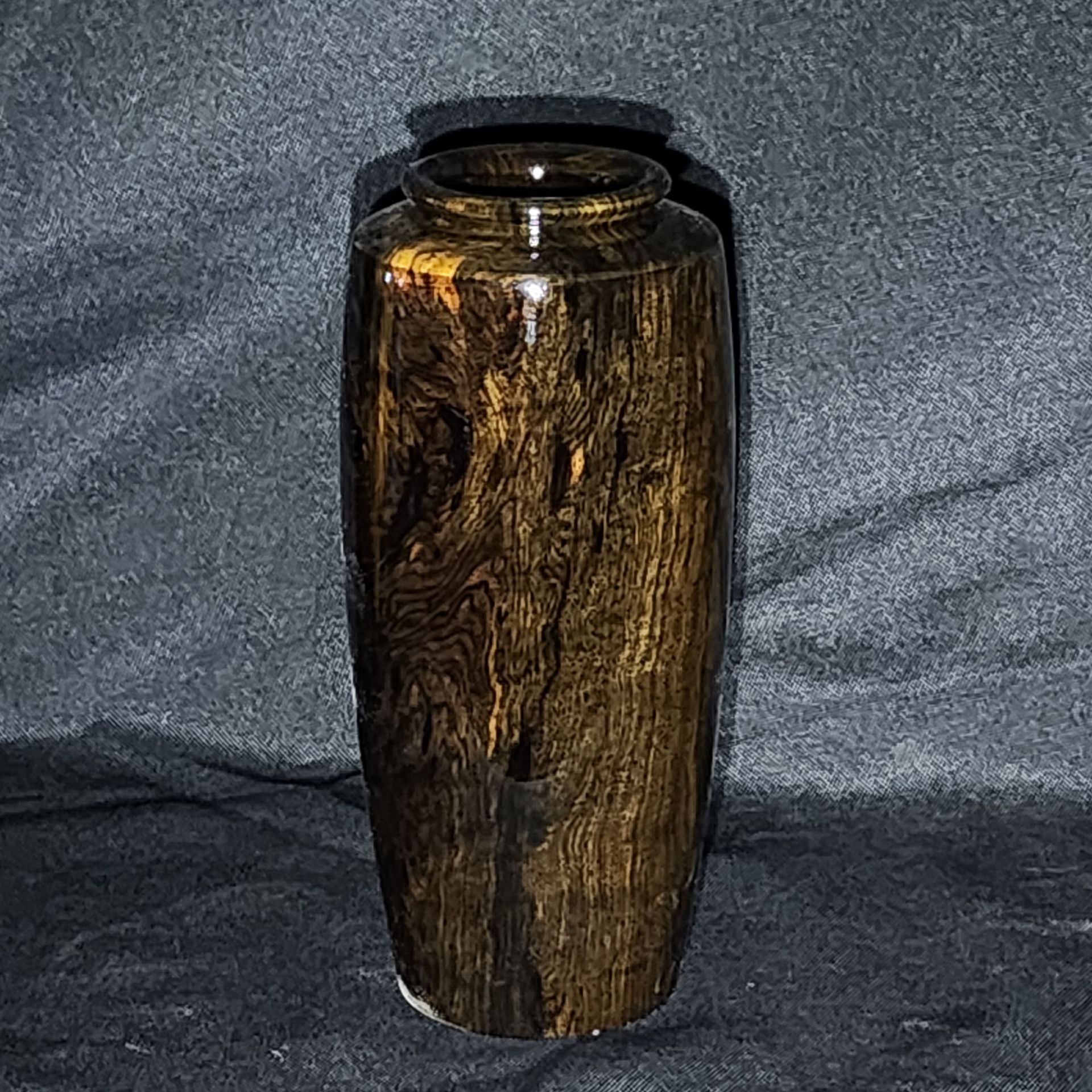 Wooden vase with orange and black patterns against a dark gray background.