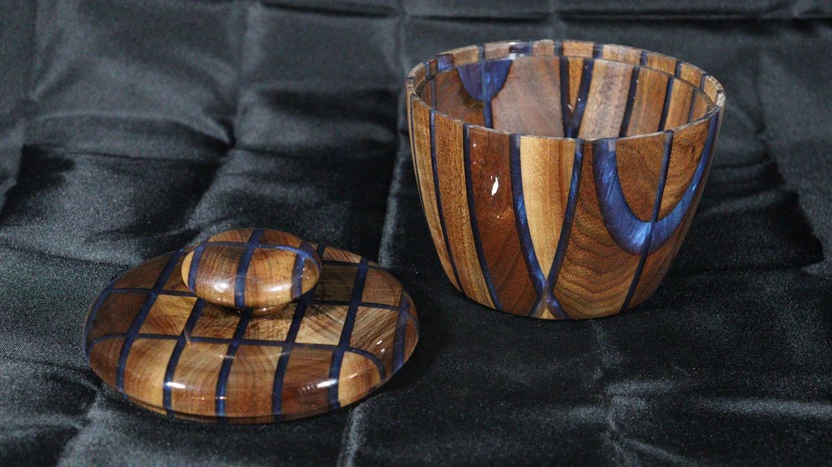 Wooden vase with three bat cutouts, filled with blue resin. Brown, on a black stand.