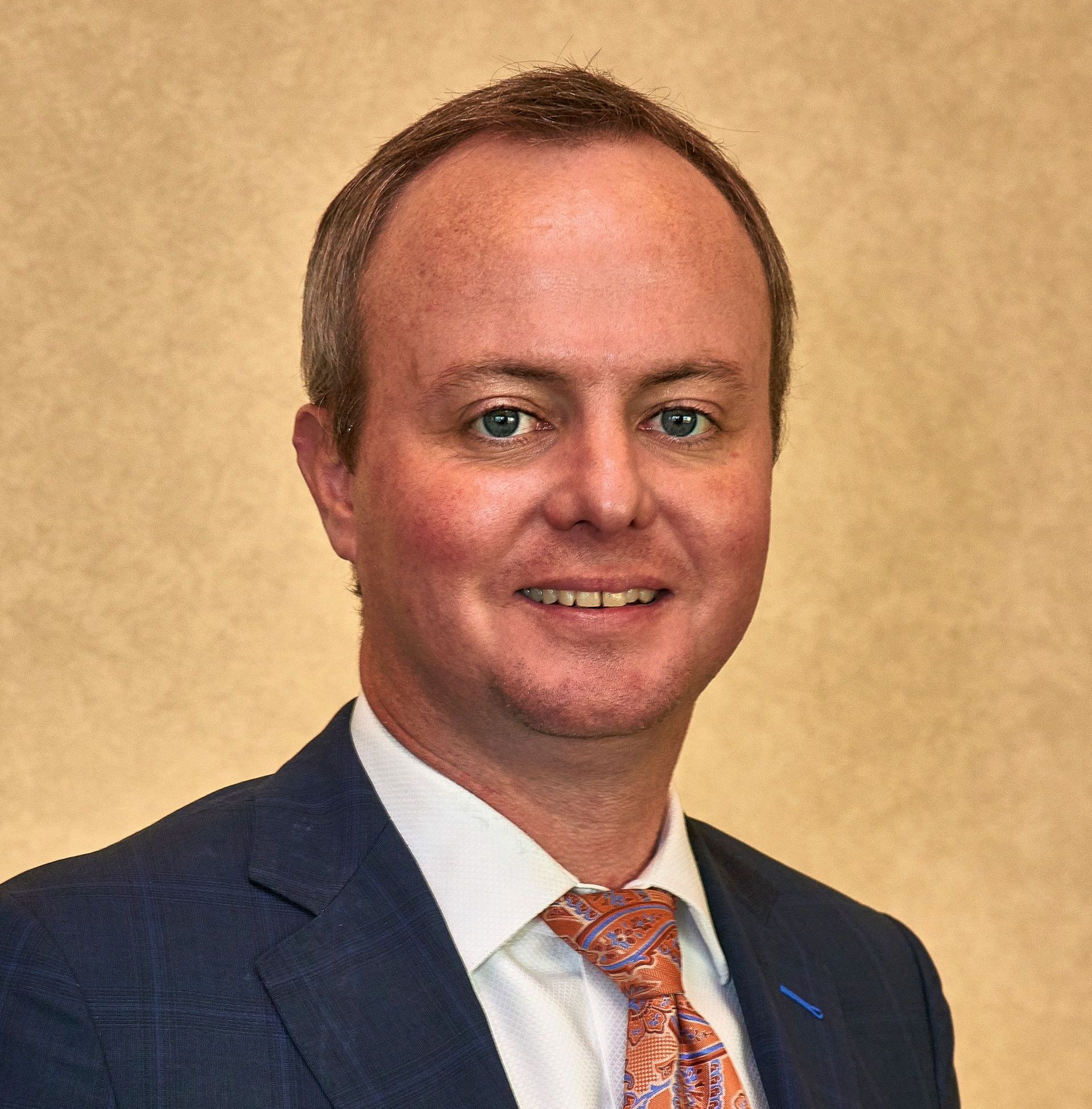 Portrait of a man in a suit and patterned tie against a beige background
