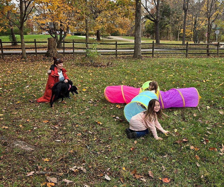 Children in autumn park, one crawling near a pink tunnel and another in a red costume by a dog