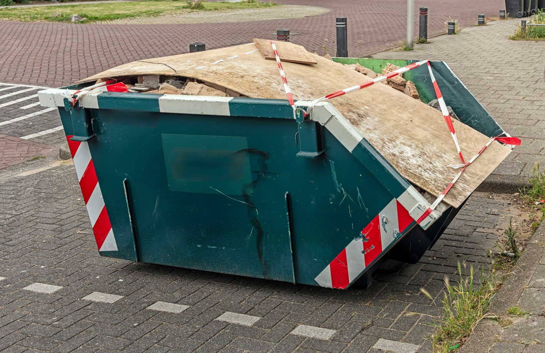 A full residential dumpster rental bin filled with construction debris on a brick driveway. A full residential dumpster rental bin filled with construction debris on a brick driveway.
