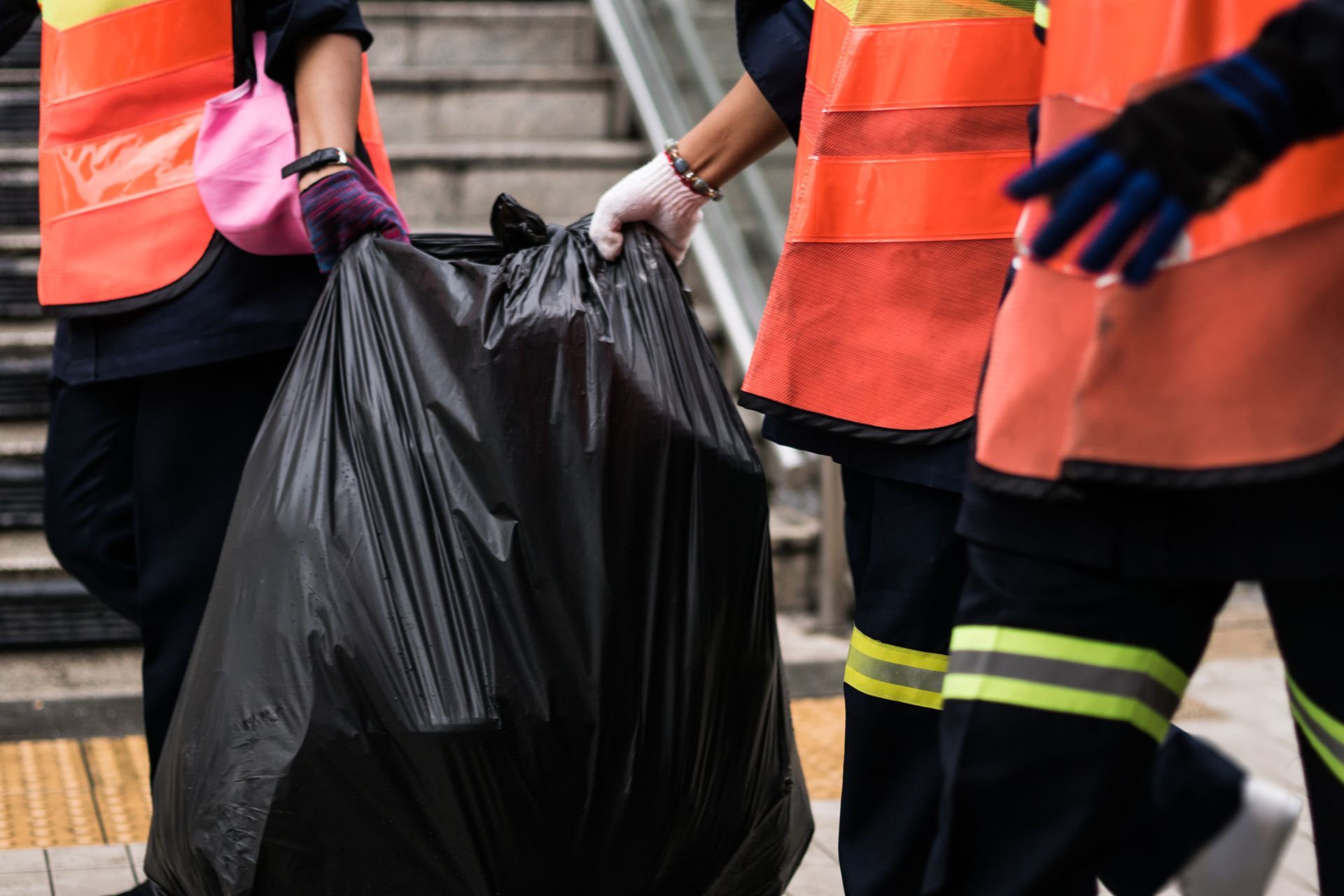 Workers in safety vests carrying a large trash bag during a community cleanup operation.