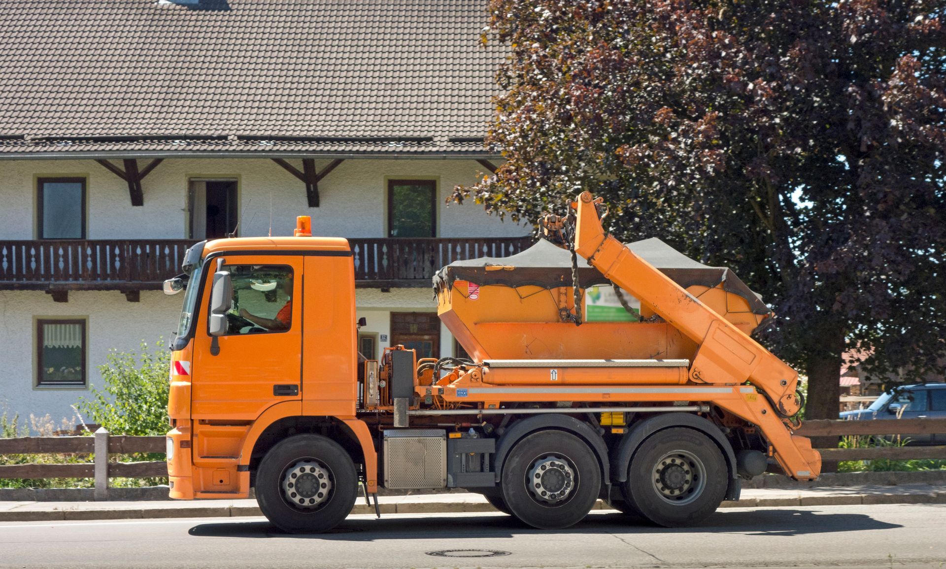 An orange dump truck is parked on a street near a residential house. An orange dump truck is parked on a street near a residential house.