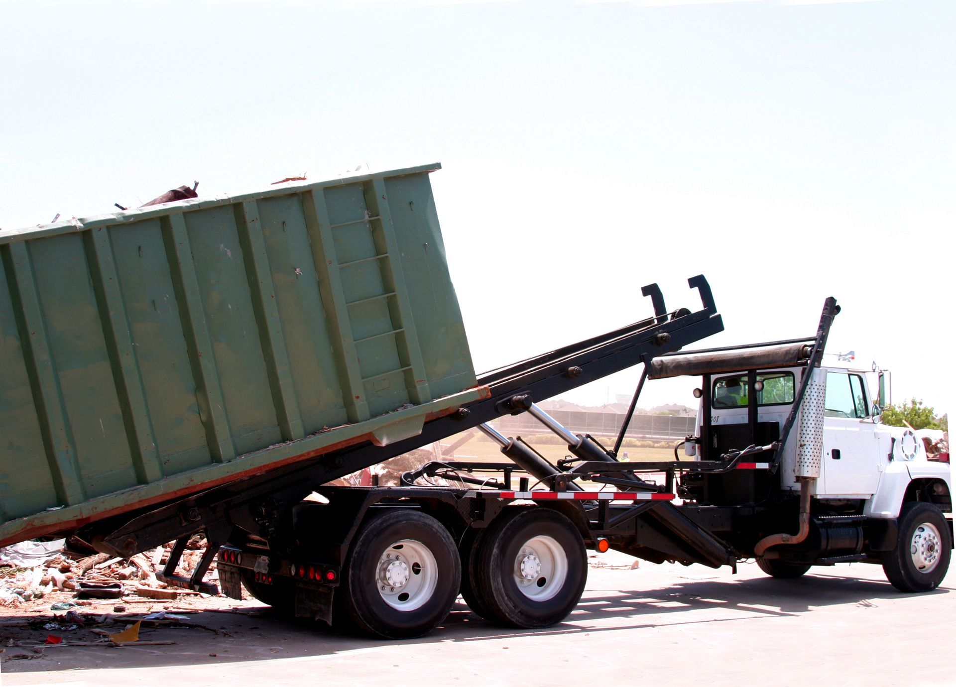 Roll off dumpster rental truck unloading debris-filled container at construction site.