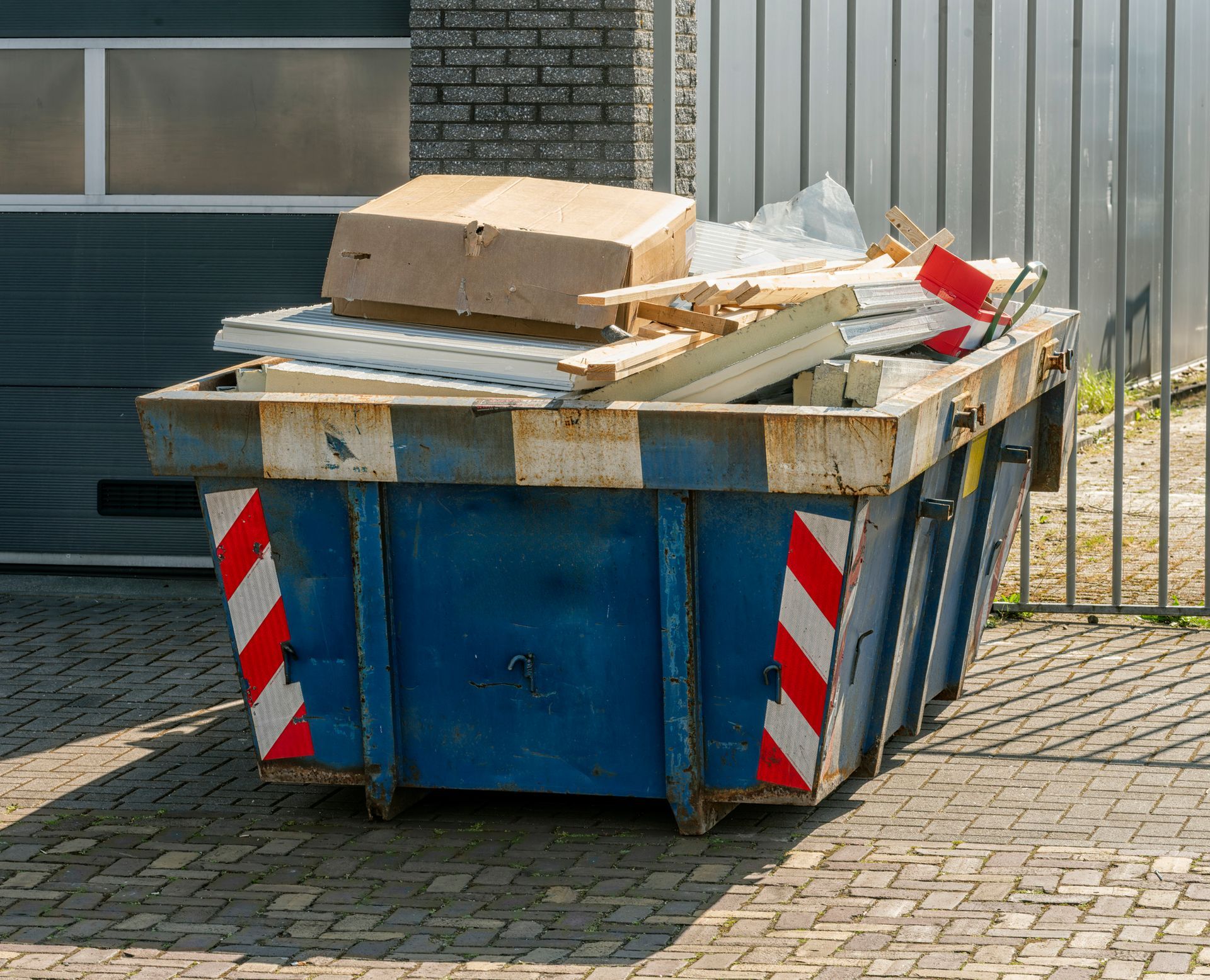 A blue dumpster filled with construction debris and cardboard.