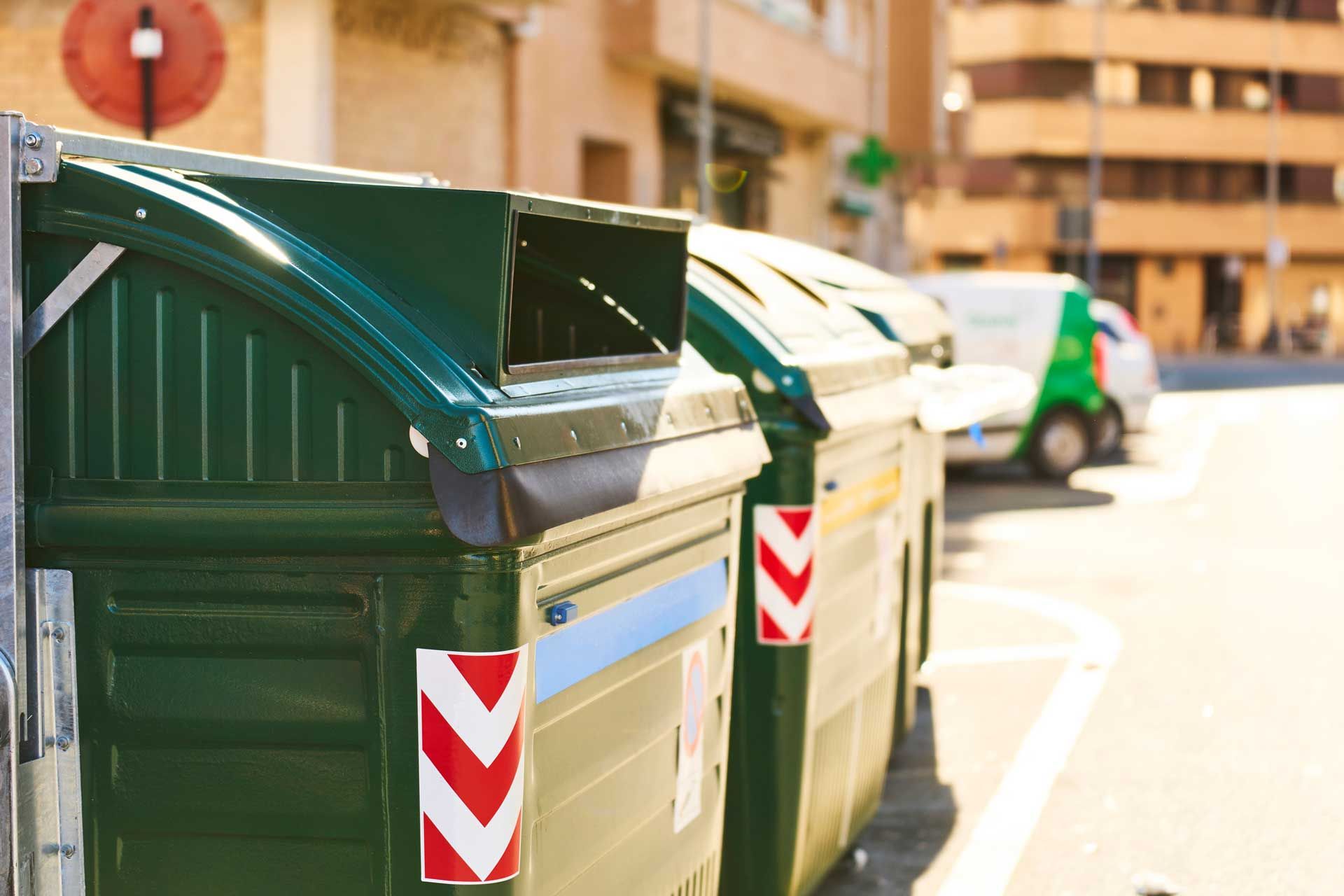 Green street bins lined up for residential dumpster rental services in a sunny urban neighborhood.
