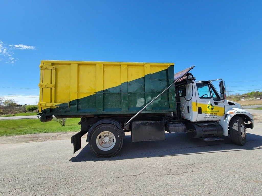 A yellow and green dump truck is parked roadside under a clear blue sky