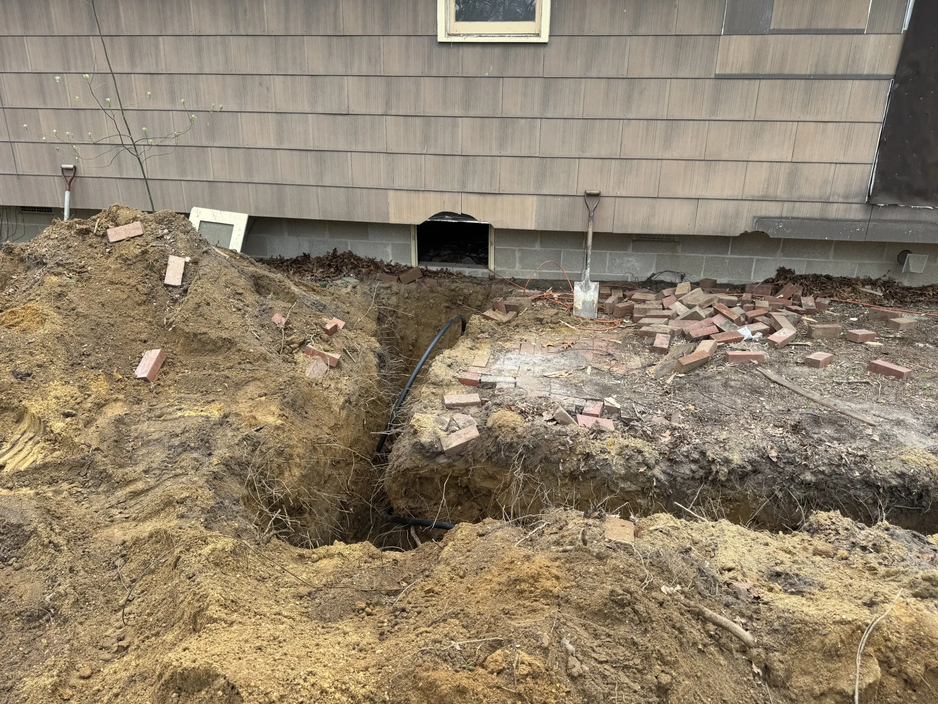 Foundation wall with a dark erosion hole and disturbed soil around a house exterior