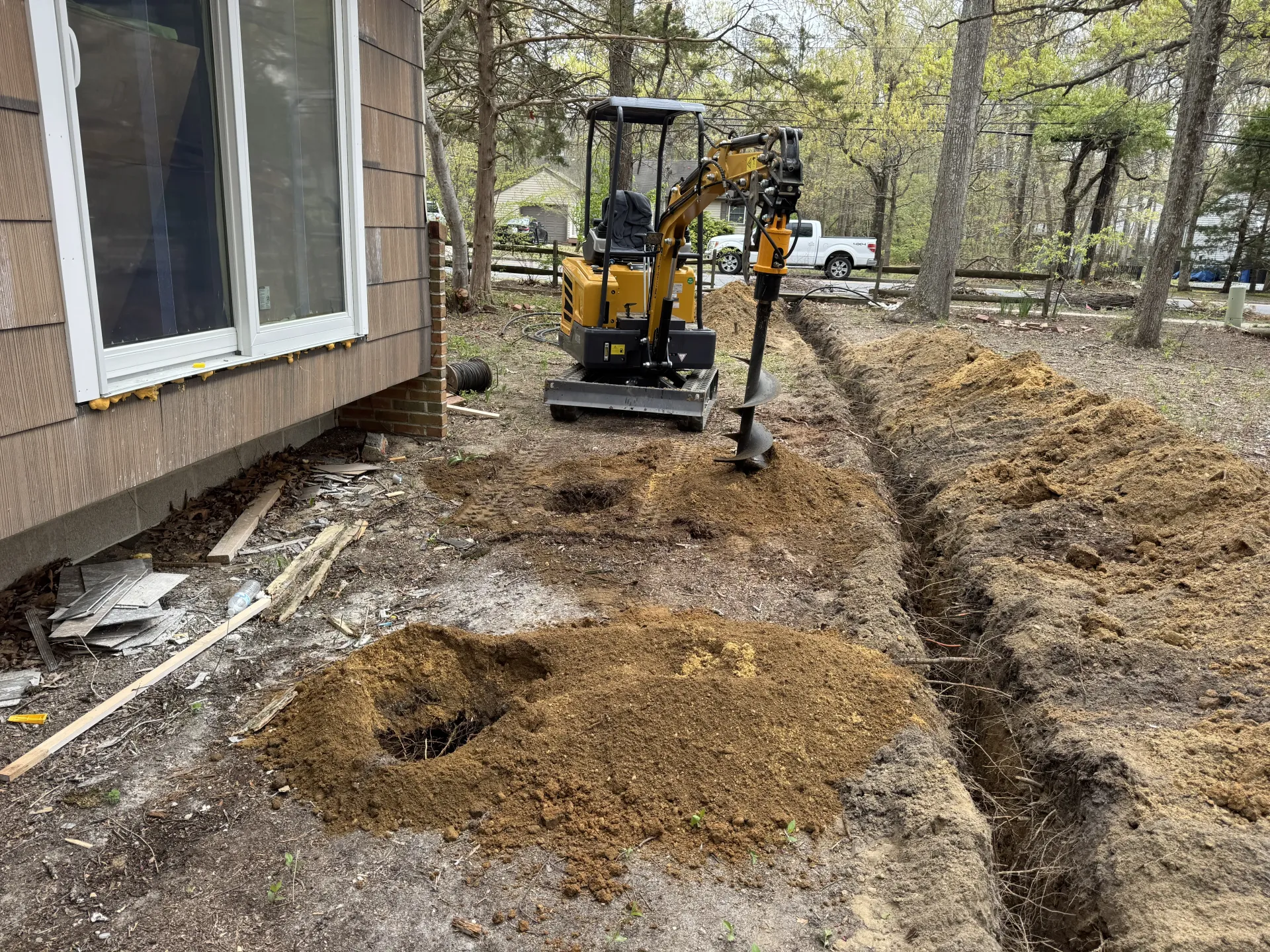 Mini excavator digging trenches beside a house in a wooded yard