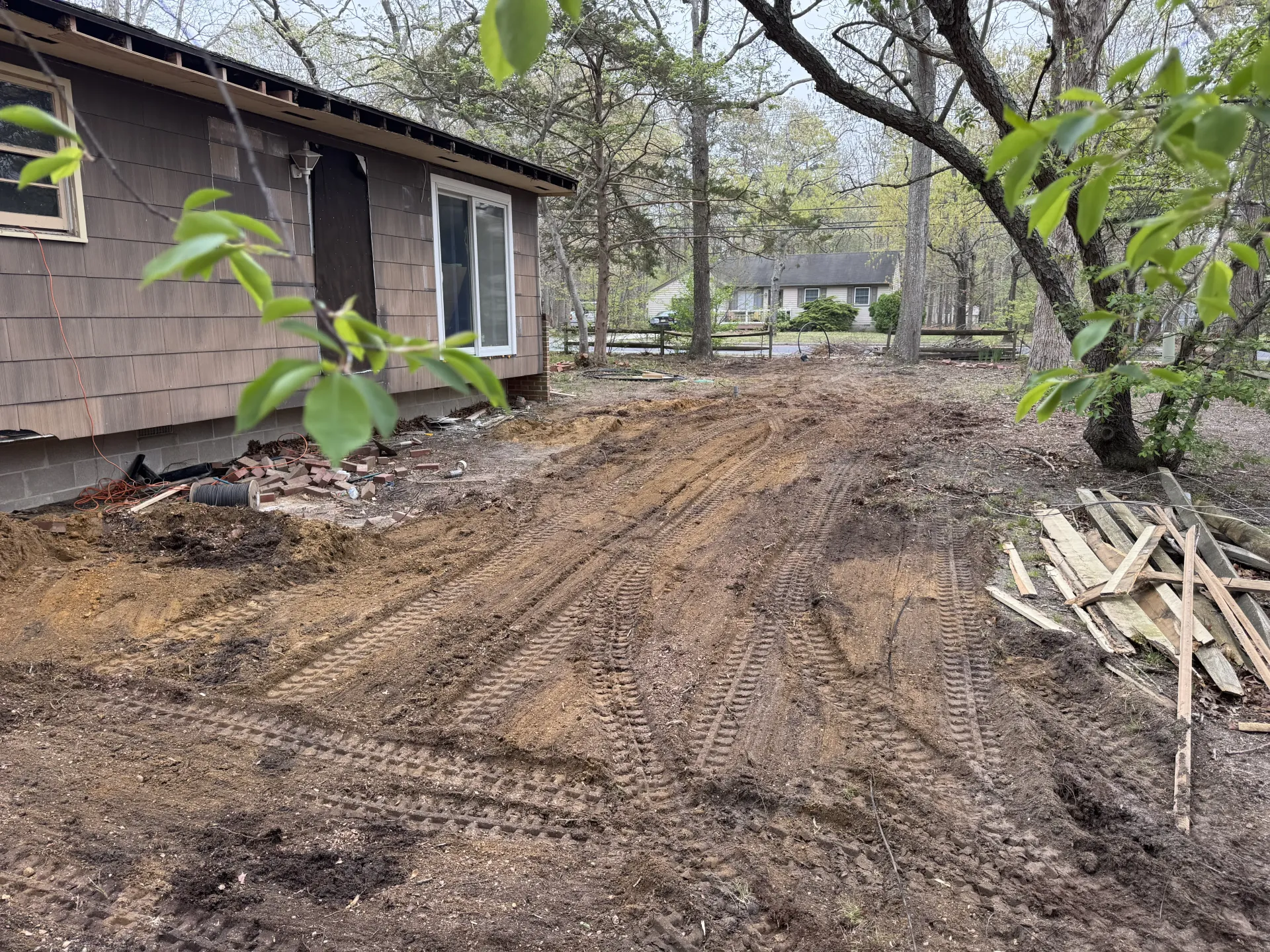 Mulched yard beside a brown house, with trees and scattered branches after clearing work