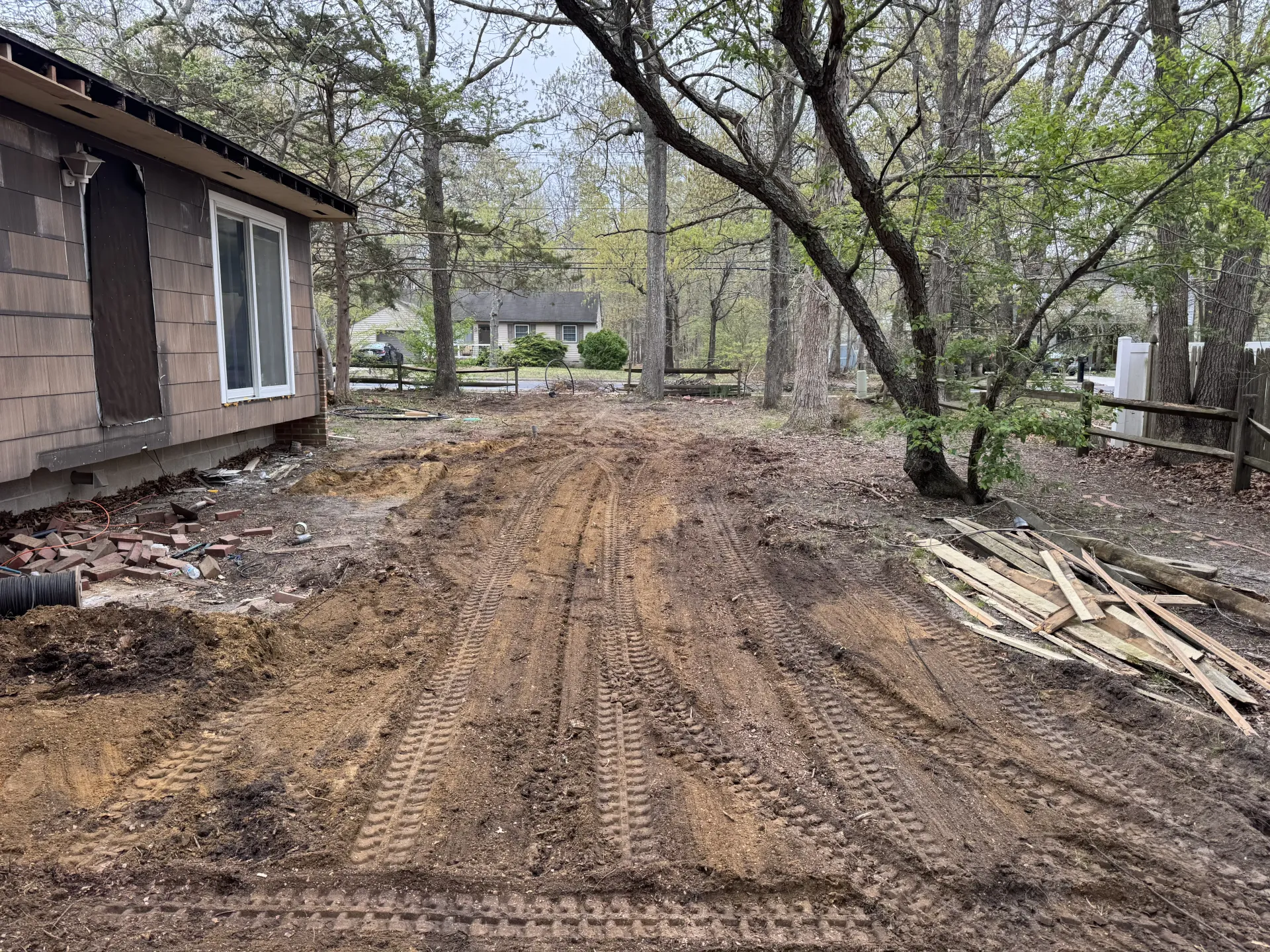 Freshly graded dirt path between a house and trees in a wooded yard