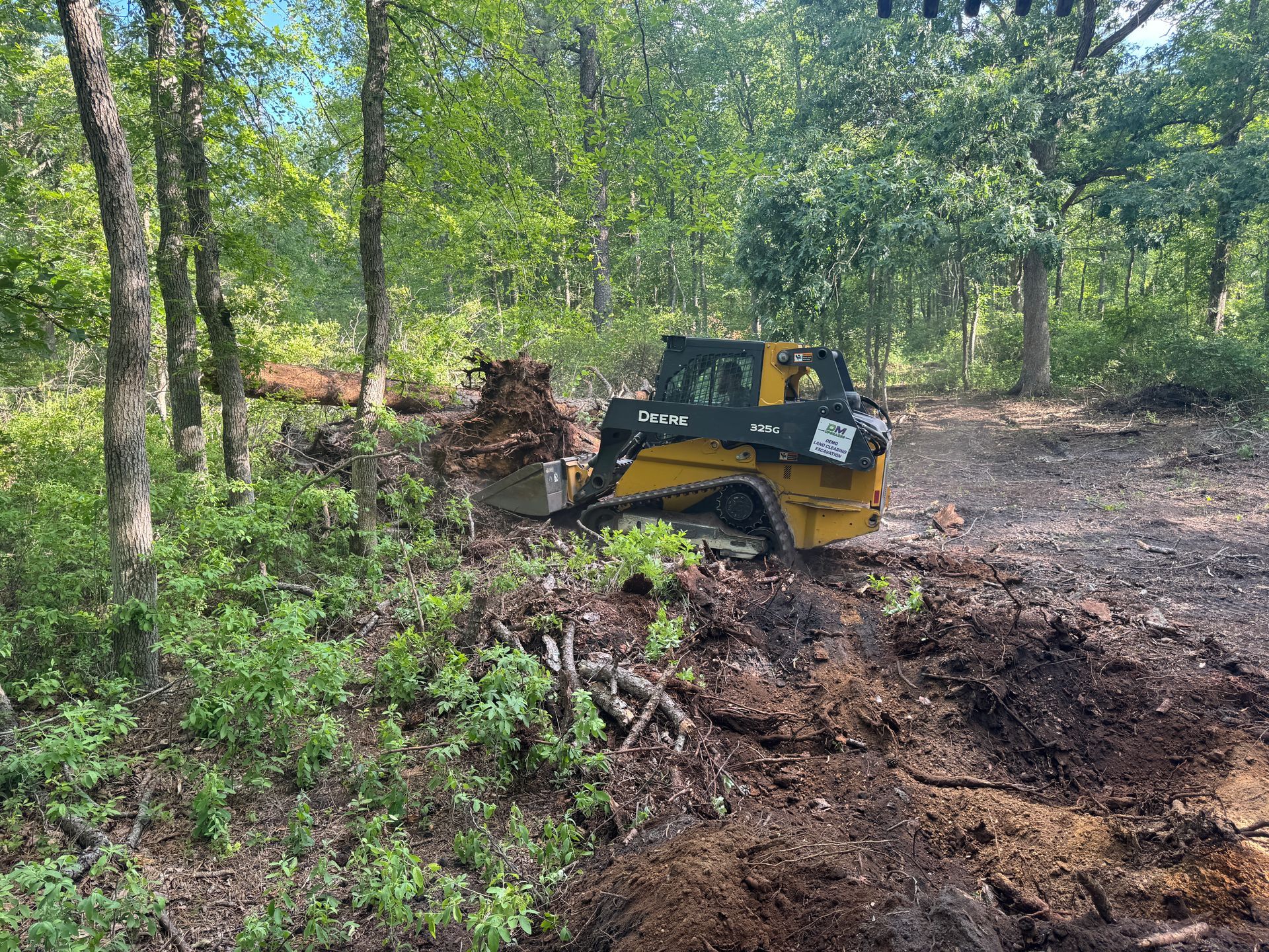 Yellow bulldozer clearing dirt in a wooded area with trees and brush nearby