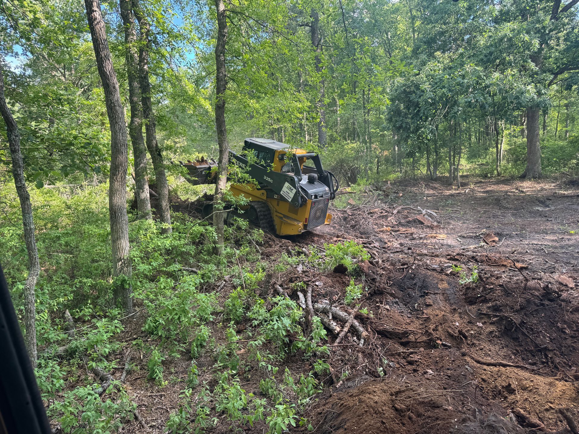 Yellow skid-steer clearing muddy ground in a wooded area