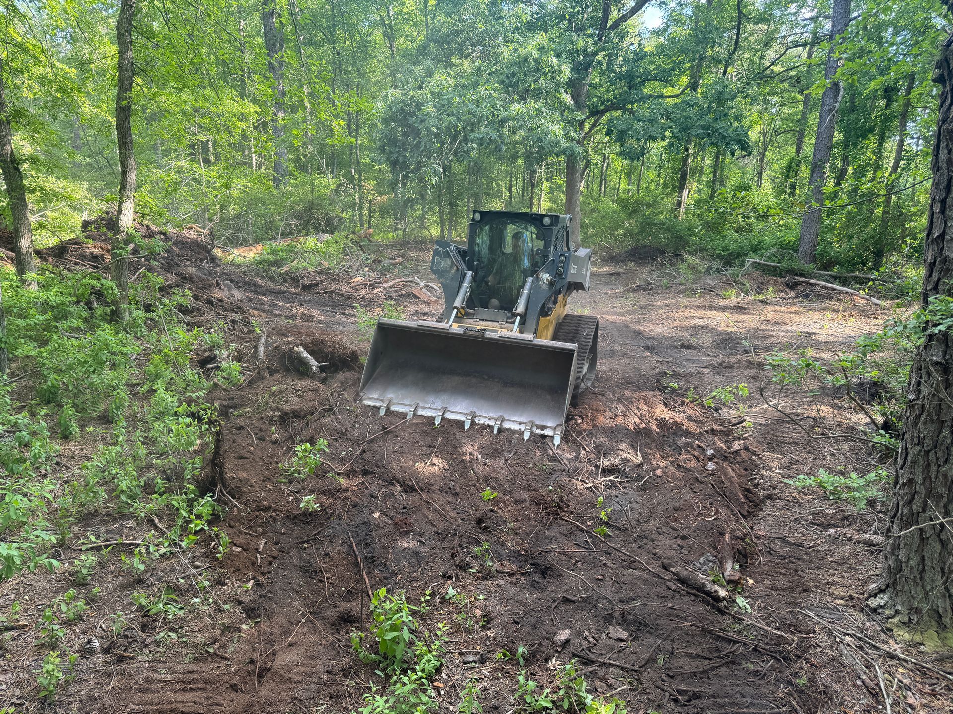 Bulldozer clearing dirt on a wooded hillside trail