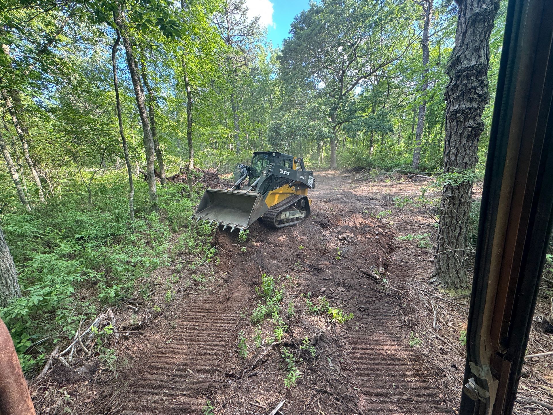 Bulldozer clearing a muddy forest path surrounded by green trees
