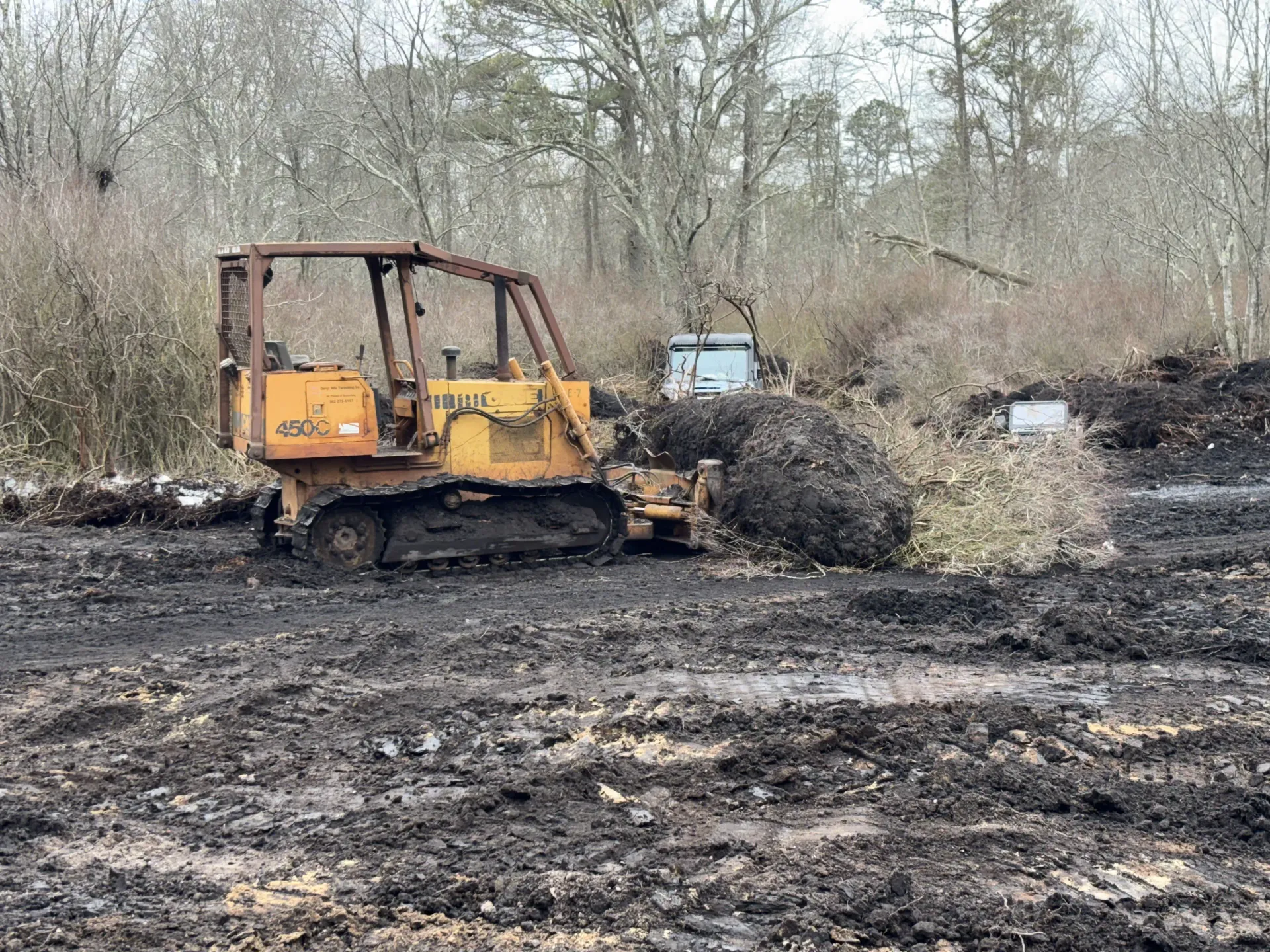 Yellow bulldozer clearing burnt debris in a muddy, charred wooded area