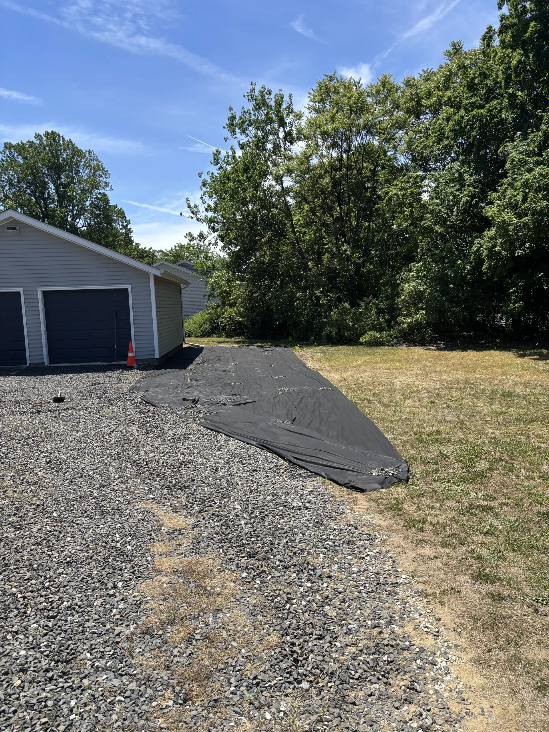 Gravel driveway beside a garage, with a black asphalt patch extending into a dry grassy yard.