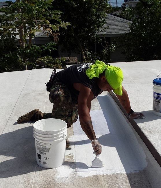 A man is working on a roof next to a bucket of paint.