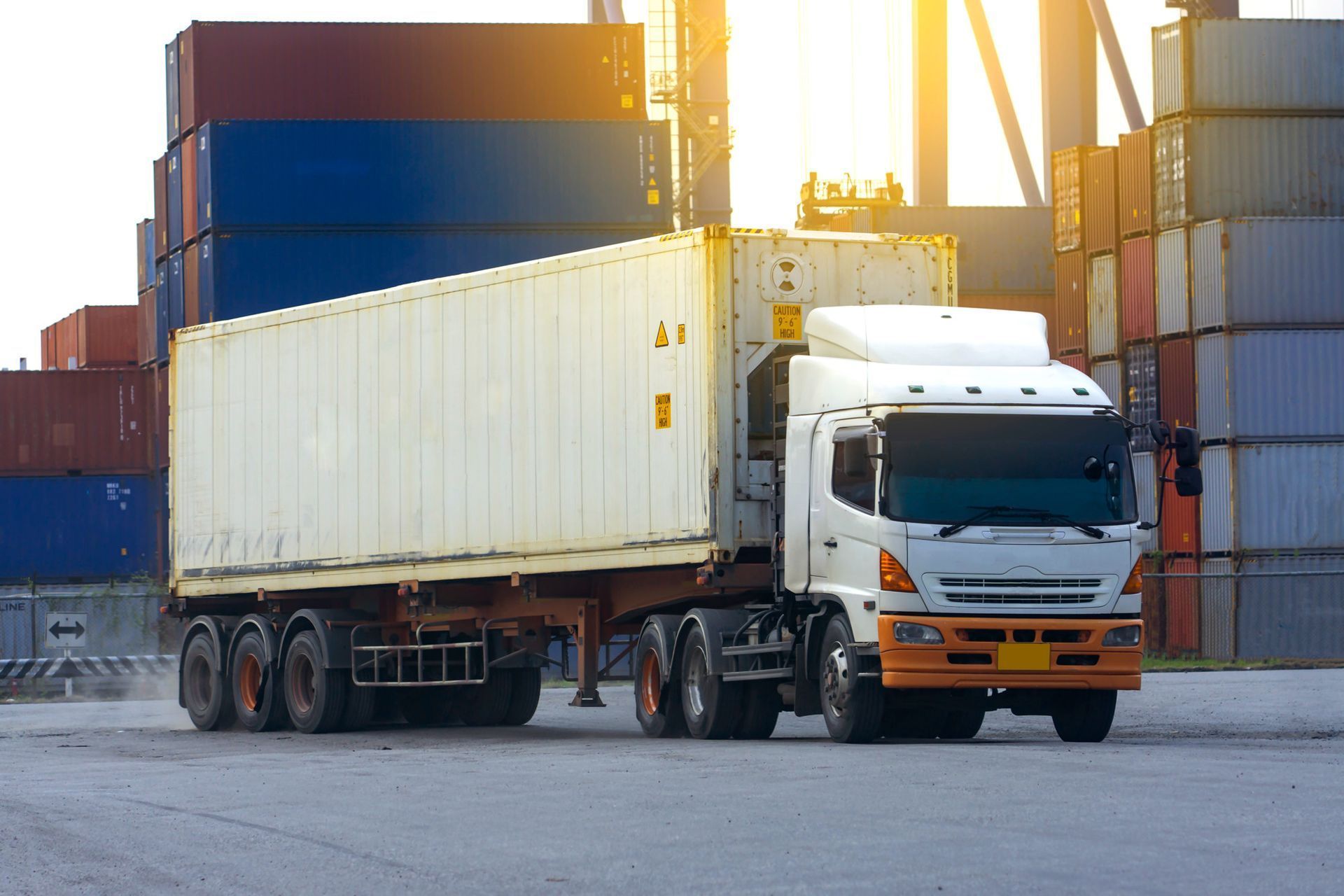 A white semi truck is driving down a road next to a row of shipping containers.