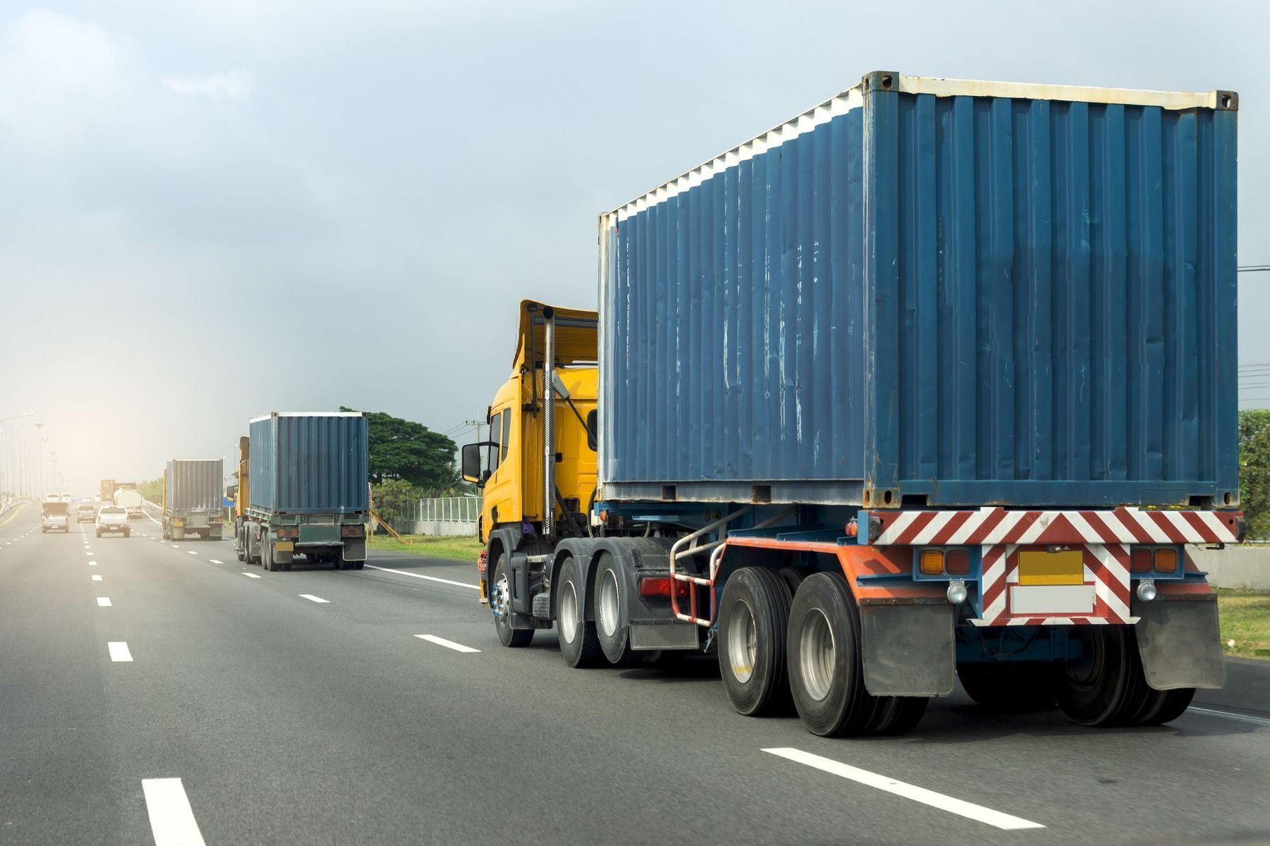 A row of semi trucks are driving down a highway.