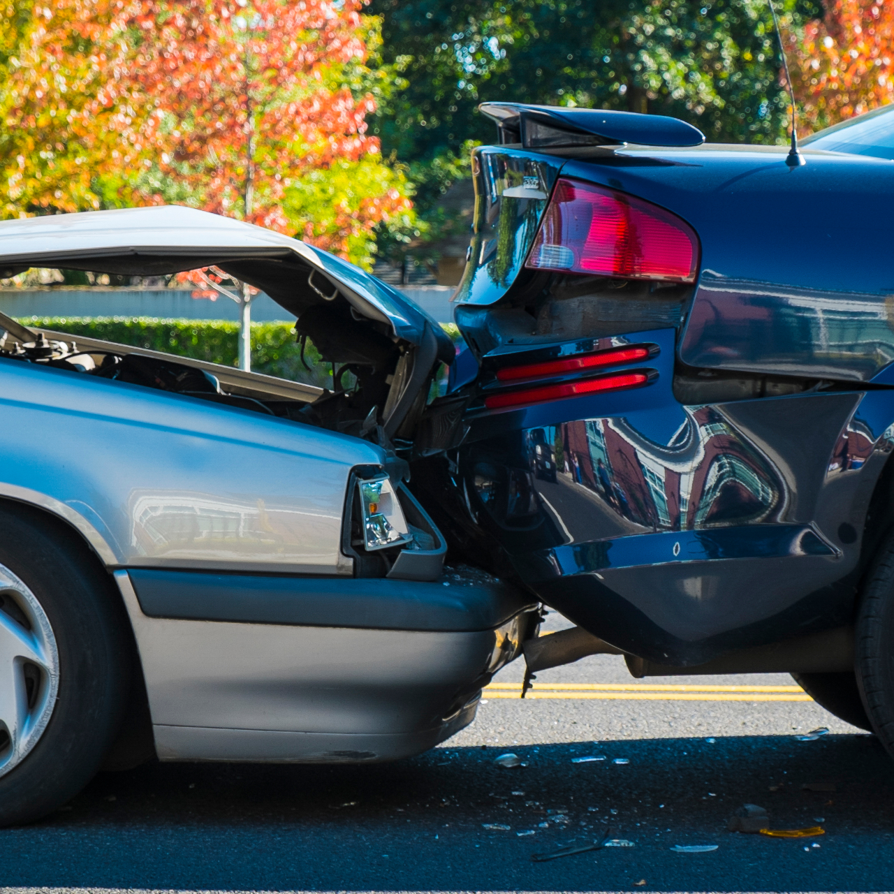 Two cars involved in a rear-end collision on a road, with a silver car's back end crumpled and a blue car's front damaged.